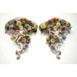 A pair of Sitzendorf porcelain wall brackets decorated in bold relief with cherubs,