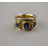 A three stone sapphire ring in matt 18ct yellow and white gold rubbed over collet setting engraved