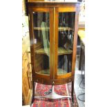 A late 19th/20th century mahogany bowfront display cabinet raised on splay legs united by a shaped