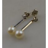 A pair of white metal and cultured pearl drop earrings hanging from a single diamond stud to/w a