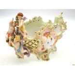 A continental porcelain rococo style reticulated bowl surmounted by three cherubs holding a garland