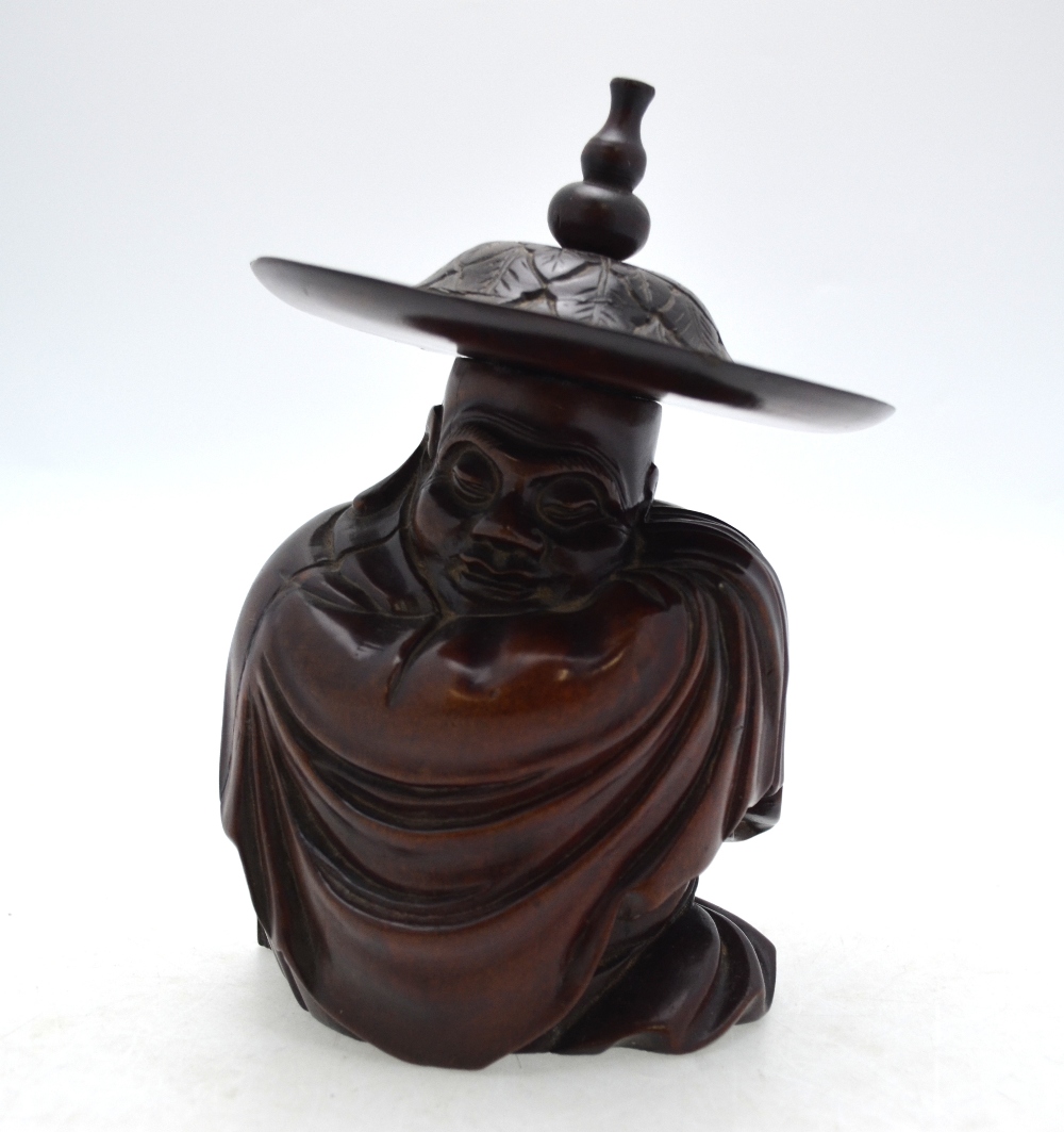 A Chinese hardwood carving of a seated sage wrapped in a cloak and wearing a wide brimmed hat,