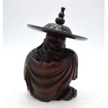 A Chinese hardwood carving of a seated sage wrapped in a cloak and wearing a wide brimmed hat,