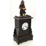 A continental mantel clock surmounted by a polychrome carved wooden seated figure of a bun eater,