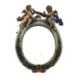 A Continental porcelain oval wall mirror decorated in relief with flowers and surmounted by two