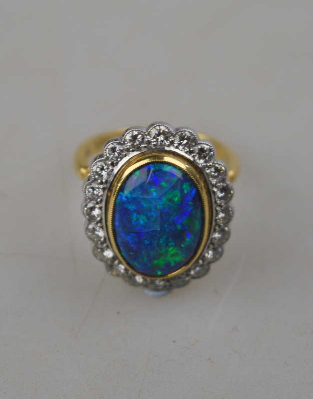 An oval black opal ring having brilliant cut diamonds around, in open basket style setting,