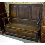 A 17th century panelled oak high back box settle with shaped arms over a hinged seat raised on