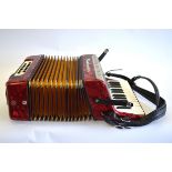 A Bandmaster red marbled piano accordion with 12 buttons,