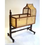 An antique mahogany framed cane panelled canopy crib, raised on a twin pillar rocking frame,