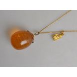 A pear-shaped amber drop suspended from a diamond-set hanger on a yellow metal curb style guard