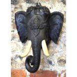 An Indian ebonised and carved wood elephant's head wall-mask with composition ivory tusks,