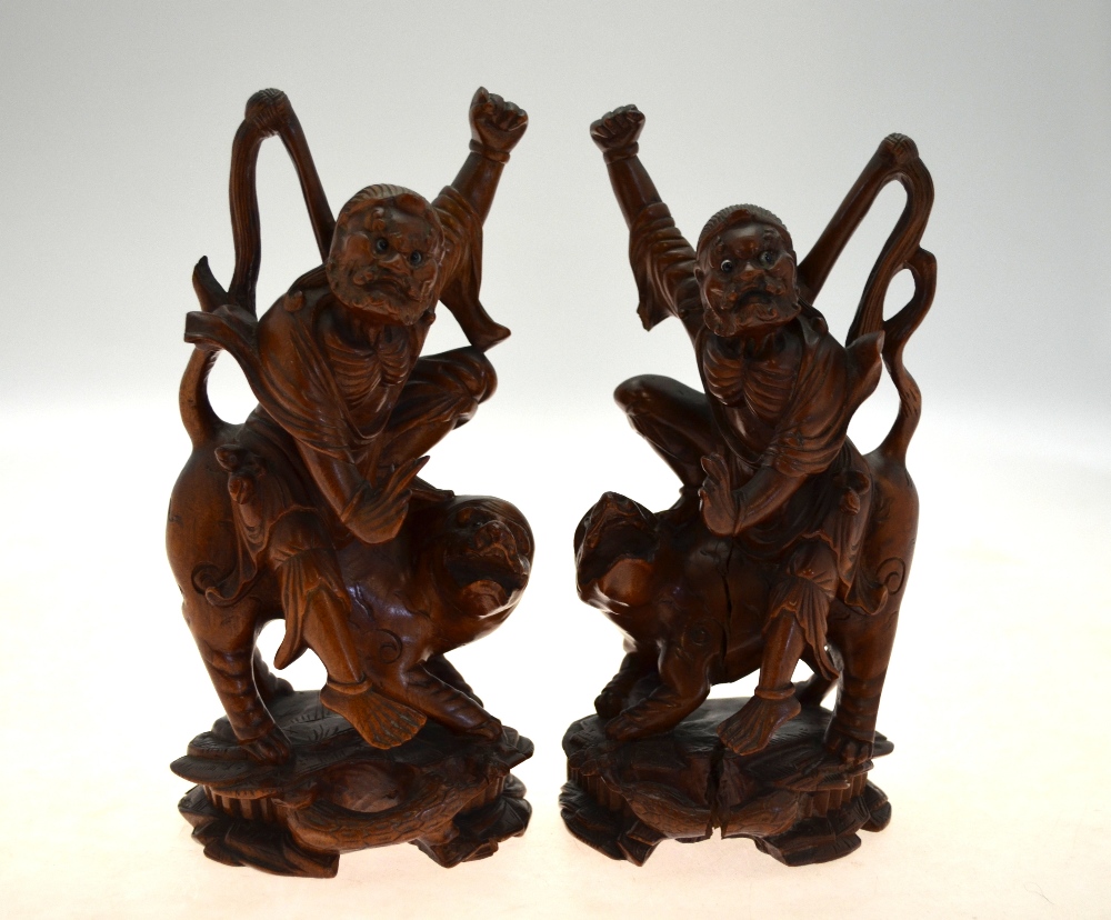 A pair of Chinese carved hardwood figures of ascetic Immortals riding a fabulous animal, 20 cm high,