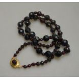 A row of facetted graduated garnet beads on yellow gold snap set with facetted garnet