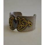 Carol Darby - a hammered silver bangle with gold scroll work having oval haematite in centre,