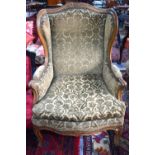 A French walnut framed wing armchair in brass studded embossed fabric with serpentine seat,