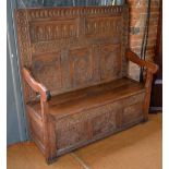 A 17th century and later carved oak box settle with panelled back over shaped arms and plank hinged