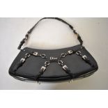 A Christian Dior black leather shoulder bag of curved form with multi-buckled strap decoration,