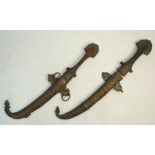 Two Arab daggers of traditional form with wooden hilts and brass mounts and scabbards,