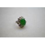 A cabochon green stone, probably jade, and diamond cluster cocktail ring, white metal set,