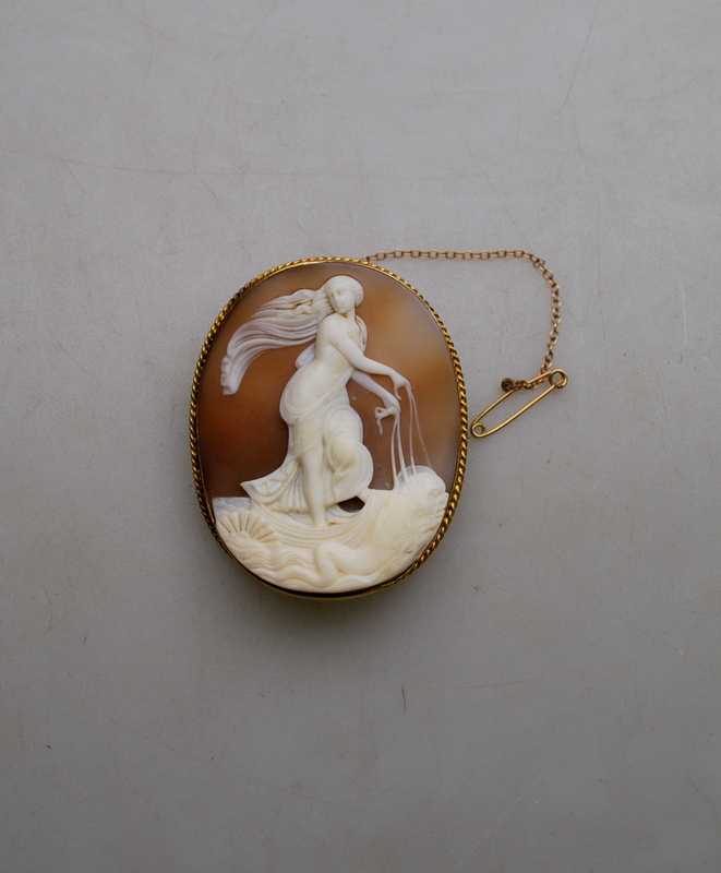 An oval shell cameo in high relief featuring classical scene in yellow gold mount stamped 15 with