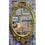 An oval carved giltwood and gesso wall mirror with shell and scroll crest and apron.