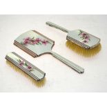 An Art Deco silver and enamel three-piece brush set, painted with pink orchids,