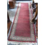A Persian runner, the repeating boteh design on red ground within floral guarded beige border, 2.