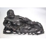 A Chinese wood figure of a recumbent figure, possibly the Daoist Liu Hai, with his cash; wood stand,