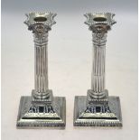 A late Victorian pair of loaded silver Corinthian column candlesticks on moulded square bases,