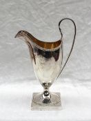 A George III silver helmet shaped cream jug, with a beaded rim, and gilt interior, on a square foot,