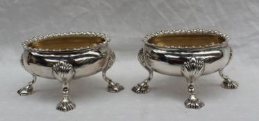 A pair of George III silver open table salts of oval form with a gadrooned edge on four shell