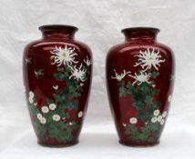 A pair of Japanese cloisonne enamel vases, decorated with chrysanthemums and leaves to a red ground,