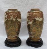 A pair of Japanese Satsuma pottery vases decorated with a village and lake in the foreground and