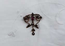 An Edwardian pink sapphire and seed pearl pendant/brooch of floral scrolling form