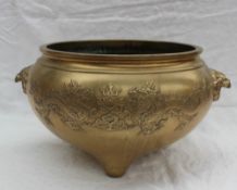 An oriental gilt bronze bowl decorated with dragons chasing a pearl with mask handles on three feet,