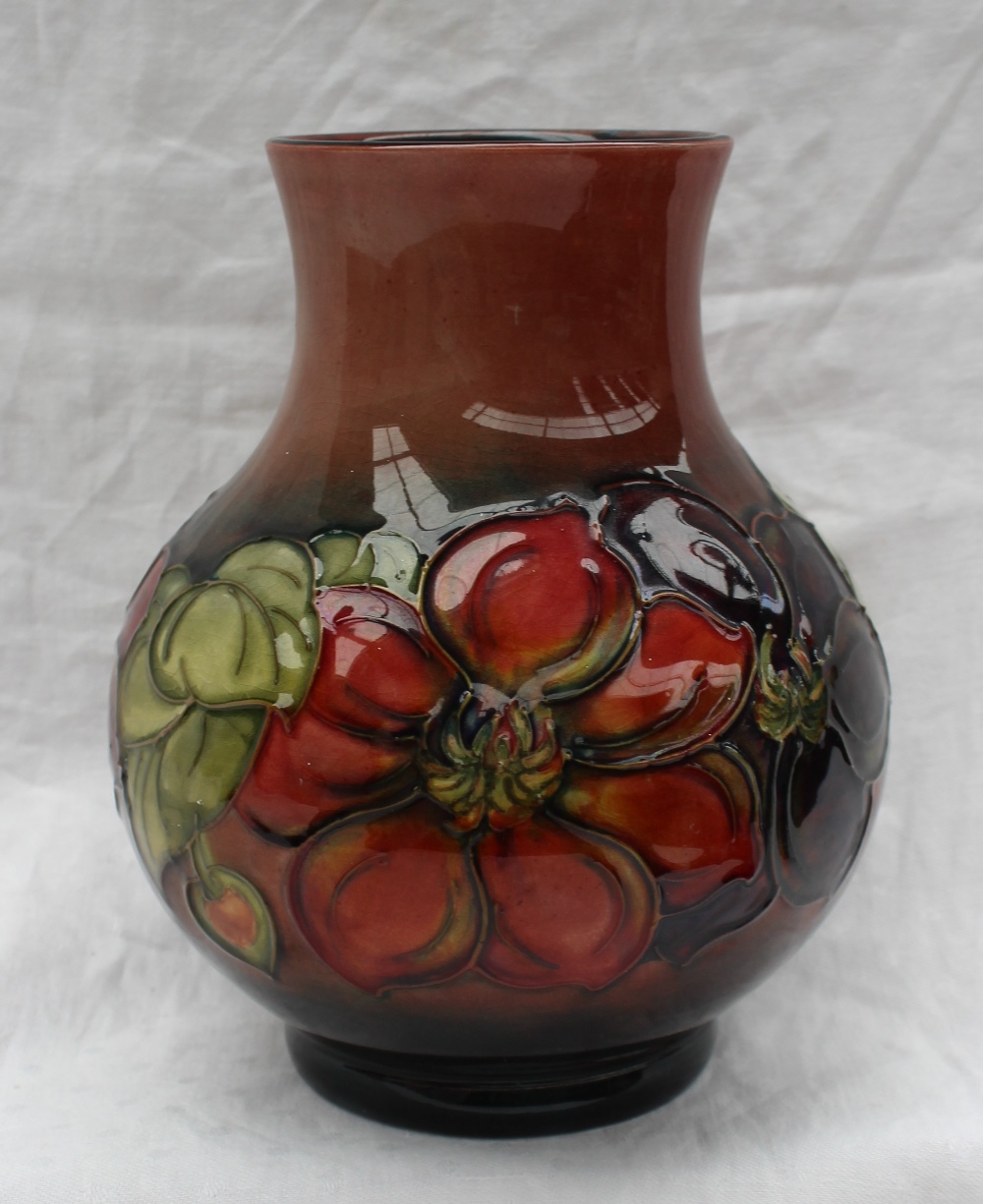 A Moorcroft vase decorated in the clematis pattern, to a graded red ground,