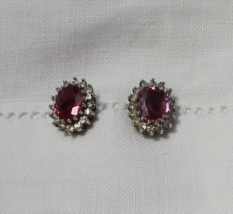 A pair of ruby and diamond cluster ear studs, each set with an oval mixed cut ruby,
