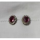 A pair of ruby and diamond cluster ear studs, each set with an oval mixed cut ruby,