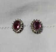 A pair of ruby and diamond cluster ear studs, each set with an oval mixed cut ruby,