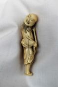 A 19th century ivory netsuke in the form of a bearded figure holding a staff and gourd over his