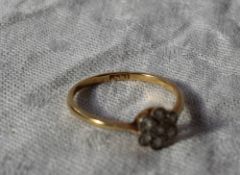 A diamond ring set with seven old cut diamonds in a daisy formation to a white metal setting and a