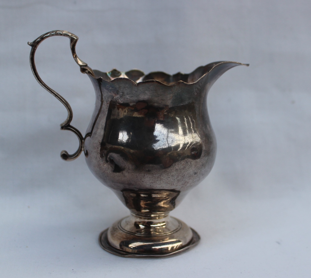 A George III silver cream jug with a flared rim and baluster body on a spreading foot, London, 1762,