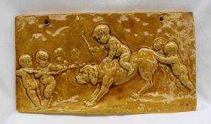 A 19th century pottery tile decorated in relief with a cherub riding a dog whilst others push and