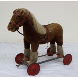 A Merrythought pull along horse with a bridle and harness with felt hooves on a metal base and