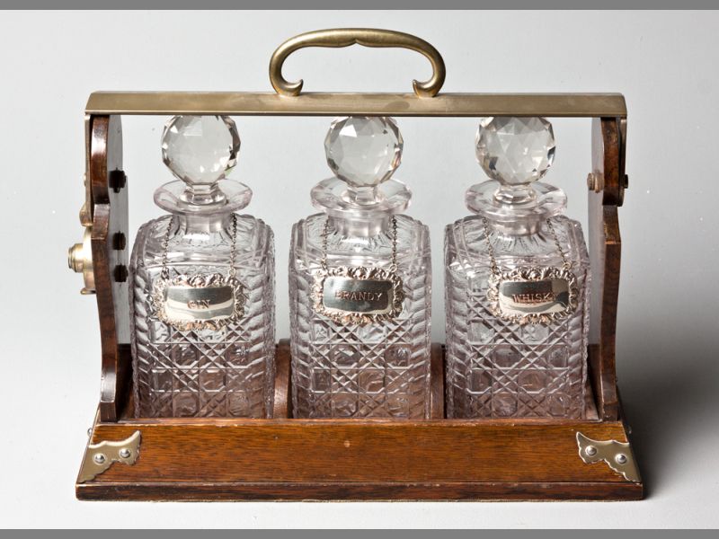 AN EARLY 20TH CENTURY THREE BOTTLE TANTALUS manufactured by BET. Emanns, London, oak cased