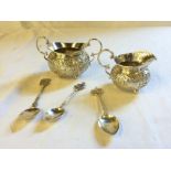 A silver sugar bowl and cream jug and three silver spoons.