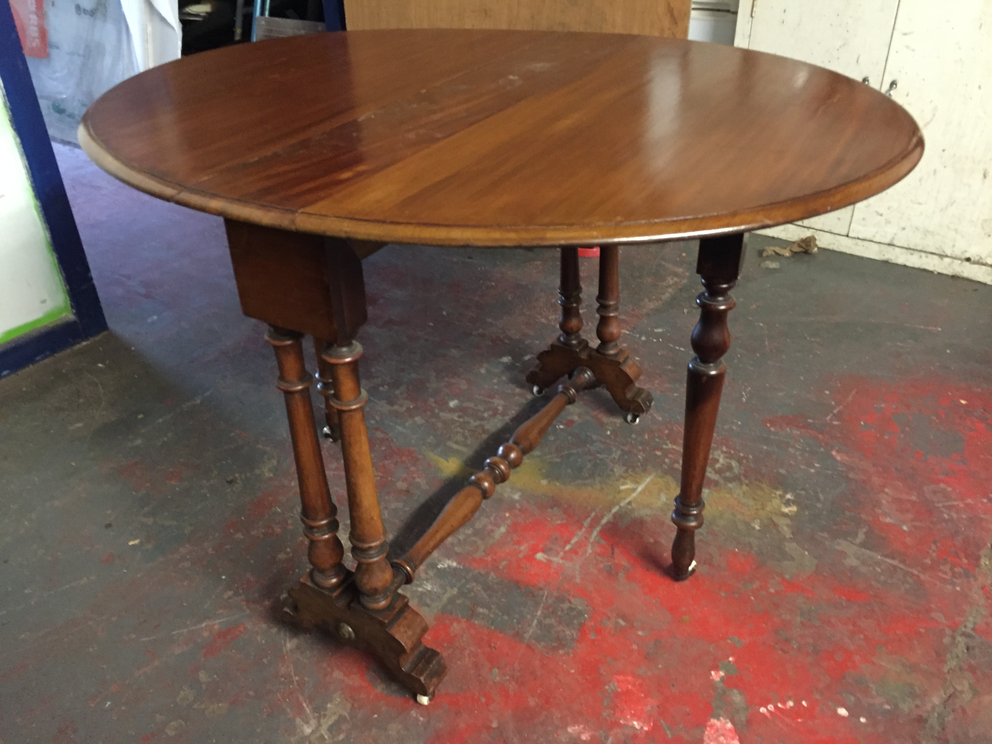 A Sutherland style circular table with turned legs and stretchers on porcelain castors.