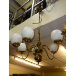 A brass electric ceiling light central rod supporting six scrolling lights and a box of six spare