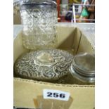 An Edwardian oval cut glass jar with embossed silver lid, a similar cylindrical jar with lid, and