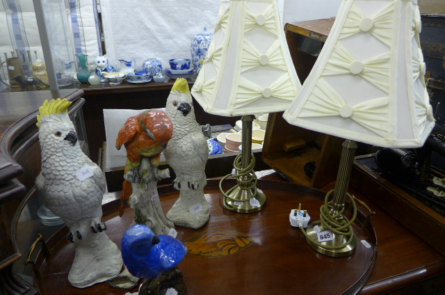 A pair of brass column table lamps, a pair of stoneware cockatoos, and a Naples figure of a parrot